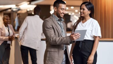 Two professionals talking at a trade show near two other employees. One of them holds a small tablet.