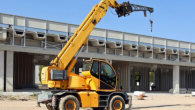 A yellow telehandler parked in the middle of a construction site. The boom arm is extended above the telehandler.