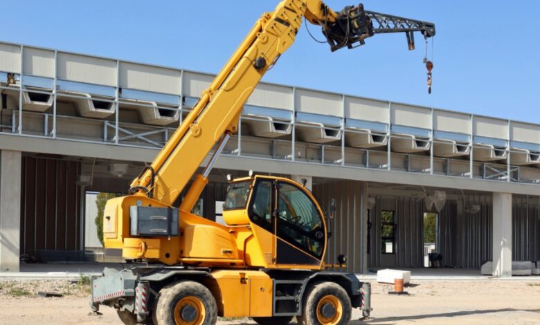 A yellow telehandler parked in the middle of a construction site. The boom arm is extended above the telehandler.
