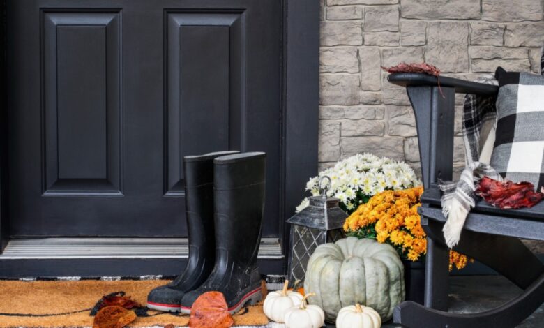 A black pair of boots on a welcome mat in front of the black front door to a home on a cloudy fall day.