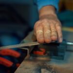 A person's hands working with a metal file to shape another piece of metal. They are working on a table.